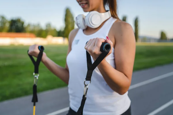 One woman training with elastic rubber resistance bands in stadium close up on hands selective focus