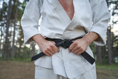 close up on hands of one man unknown karateka holding karate black belt wear white kimono gi in the forest in nature in day martial arts concept skill master