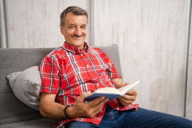 One man senior caucasian male with mustaches read book at home wear red shirt real people leisure concept copy space happy smile looking to the camera