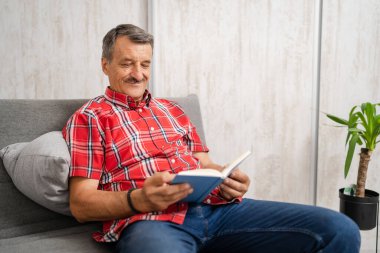 One man senior caucasian male with mustaches read book at home wear red shirt real people leisure concept copy space