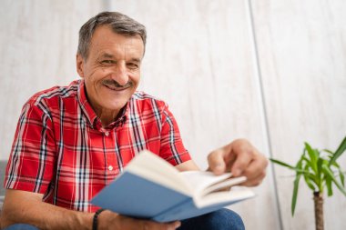 One man senior caucasian male with mustaches read book at home wear red shirt real people leisure concept copy space looking to the camera happy smile
