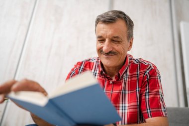One man senior caucasian male with mustaches read book at home wear red shirt real people leisure concept copy space