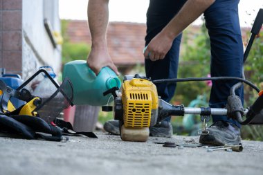 Young farmer adding petrol gas to the gasoline tank of the brushcutter string trimmer