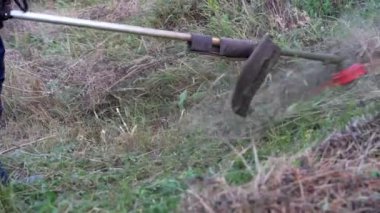 Young caucasian man farmer gardener standing in the field with string trimmer petrol Brushcutter cut weed grass working on farm cutting in the field in sunny day by the house in the village