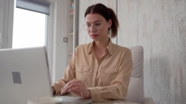 One woman female caucasian entrepreneur businesswoman or secretary sitting at her office at desk work on laptop computer typing happy smile wear shirt and eyeglasses work on project and documents