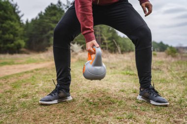 One unknown caucasian man in the field in nature training with girya kettlebell weight alone health and fitness exercise confident male lifting weights health and fitness concept copy space midsection