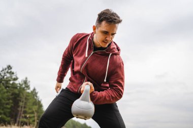 One caucasian man in the field in nature training with girya kettlebell weight alone health and fitness exercise confident male lifting weights health and fitness concept copy space real people