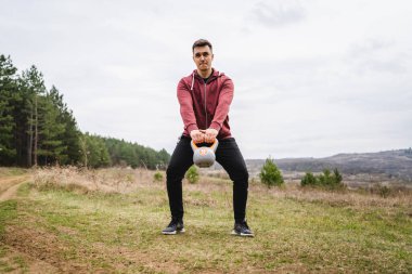 One caucasian man in the field in nature training with girya kettlebell weight alone health and fitness exercise confident male lifting weights health and fitness concept copy space real people