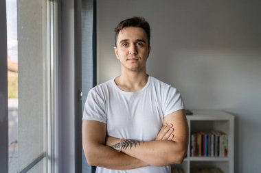 One man young adult male caucasian with brown hair standing by the window at home in day confident looking to the camera wear white shirt real people copy space