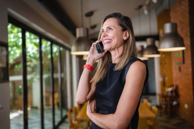 One woman middle age caucasian female standing at home happy smile confident wear black waist up copy space front view portrait using mobile phone making a call talking confident
