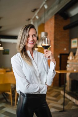One woman middle age caucasian female standing at home in dining room or restaurant happy smile confident with glass of red wine wear white shirt waist up copy space front view portrait