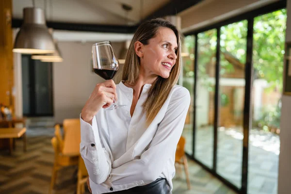 One woman middle age caucasian female standing at home in dining room or restaurant happy smile confident with glass of red wine wear white shirt waist up copy space front view portrait