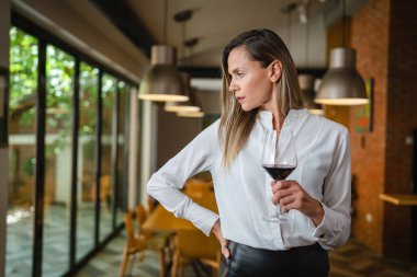 One woman middle age caucasian female standing at home in dining room or restaurant happy smile confident with glass of red wine wear white shirt waist up copy space front view portrait