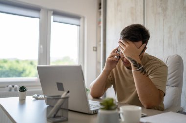 One man caucasian male sit in the office at work at desk use mobile phone to make a call while working on project wear eyeglasses talking consulting copy space real people hold head solving problems