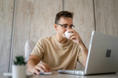 One caucasian man sit at office at work working on laptop computer in day young freelance or entrepreneur businessman read mail online business copy space young adult hold cup of coffee drink