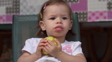 One girl small caucasian toddler child eat pear while sit outdoor copy space wear white dress looking curious alone growing up childhood development concept