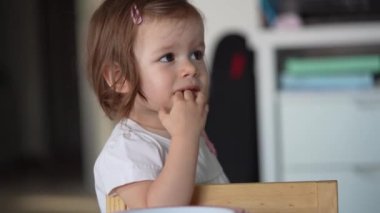 One girl small caucasian toddler child eat bread at home copy space wear white dress looking curious alone growing up childhood development concept
