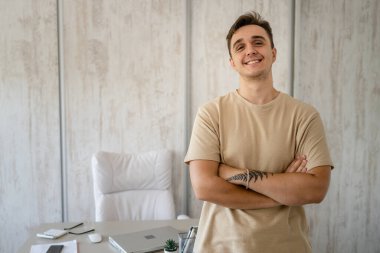 One man adult caucasian male standing in front of table desk at work in the office or work from home wear shirt looking confident casual happy smile copy space real people freelance work