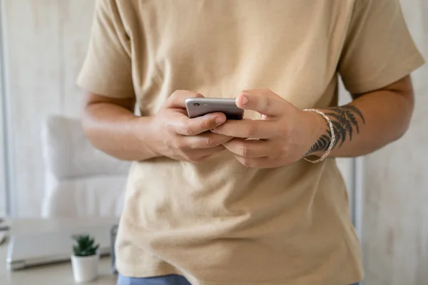 Close up on hands of unknown caucasian man standing in the office or at home in day using mobile phone to make a call or send sms text message or browse internet social network