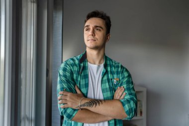 One man young adult male caucasian with brown hair standing by the window at home in day confident looking to the side wear green shirt real people copy space