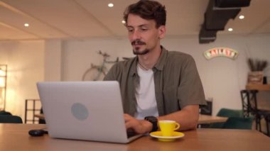 One adult modern man caucasian male with beard and mustaches wear causal shirt working remote from cafe freelance work or blog checking online content or browsing internet while sitting alone