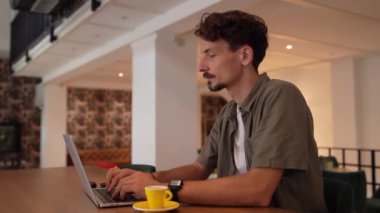 One adult modern man caucasian male with beard and mustaches wear causal shirt working remote from cafe freelance work or blog checking online content or browsing internet while sitting alone