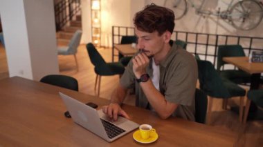 One adult modern man caucasian male with beard and mustaches wear causal shirt working remote from cafe freelance work or blog checking online content or browsing internet while sitting alone