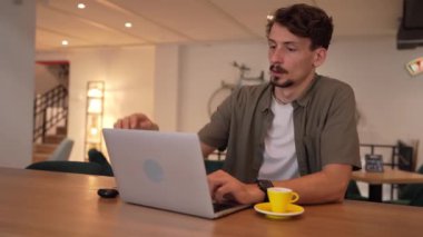 one man young adult caucasian male sitting at the table at cafe working on his laptop computer remote having headache and eyestrain due to overwork freelancer eyesight problem holding head