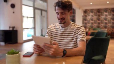 one caucasian man young adult millennial male using digital tablet while sitting in cafe at the table alone happy smile confident having online chat using internet for text messages or social network