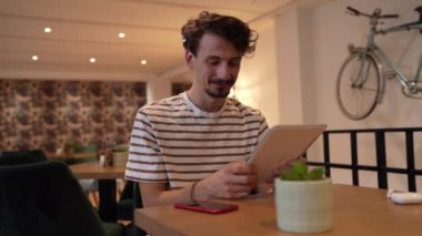 one caucasian man young adult millennial male using digital tablet while sitting in cafe at the table alone happy smile confident having online chat using internet for text messages or social network