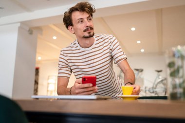 one caucasian man young adult millennial male using mobile phone stand at table in cafe at the table alone happy smile confident having online chat using internet for text messages or social network