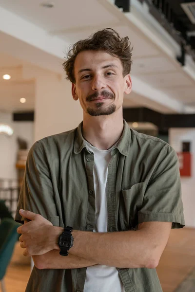 One man front view portrait waist up standing indoor in cafe or restaurant lobby happy smile confident wear olive shirt with modern haircut mustaches and beard looking to the camera