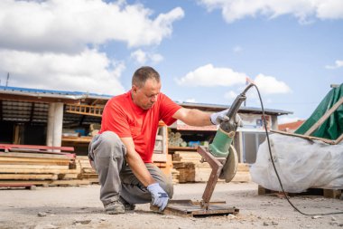 One man caucasian male construction or warehouse worker cutting iron armature construction material with grinder in sunny summer day copy space real person
