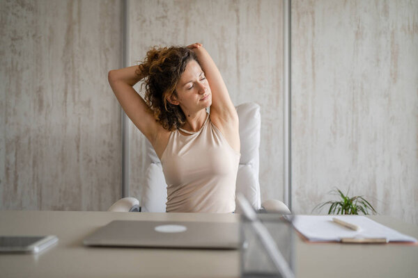 One woman freelancer stretch while sitting at work sitting in chair at desk using laptop computer having pain sore back suffering from neck ache overwork and exhaustion concept copy space