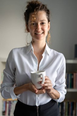 Bir iş kadını genç yetişkin kadın Kafkasyalı sabah ofiste duruyor. Kendine güler yüzlü, bir fincan kahve fotokopisi alan.