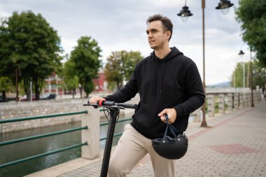 Yetişkin bir beyaz adam şehirde ya da kasabada elektrikli scooter kullanıyor ya da ayakta duruyor. Gerçek insanlar uzay çevre dostu ulaşım modelini taklit ediyor.