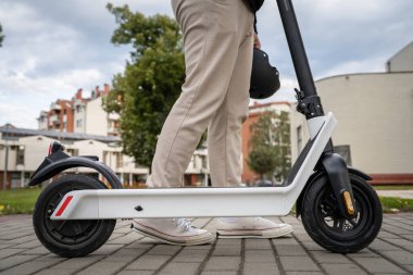 Kimliği belirsiz bir adam ayakta duruyor ya da elektrikli scooter kullanıyor. Gündüz vakti kaldırımda e-scooter kullanıyor. Çevre dostu modern ulaşım.