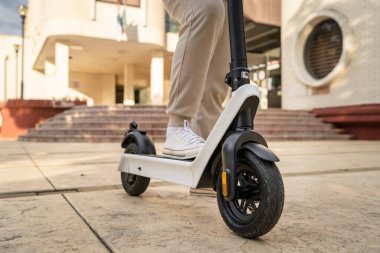 Kimliği belirsiz bir adam ayakta duruyor ya da elektrikli scooter kullanıyor. Gündüz vakti kaldırımda e-scooter kullanıyor. Çevre dostu modern ulaşım.