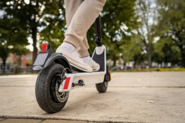 Kimliği belirsiz bir adam ayakta duruyor ya da elektrikli scooter kullanıyor. Gündüz vakti kaldırımda e-scooter kullanıyor. Çevre dostu modern ulaşım.