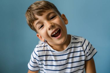 Kafkasyalı bir çocuk mavi duvarın önünde evde aylak aylak dolaşıp çocukluk portresi çiziyor.