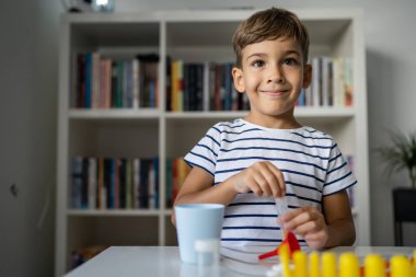 Anaokulundan bir çocuk bilim deneyi oyuncaklarıyla masada oturuyor. Kameraya bakıyor. Gülümseyen çocukluk dönemi konsepti.