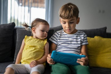 Anaokulundan bir çocuk, küçük kız kardeşiyle birlikte evde oturup dijital tablete bakarak oyun oynayarak büyüyen kardeşlerinin konseptini öğreniyor.