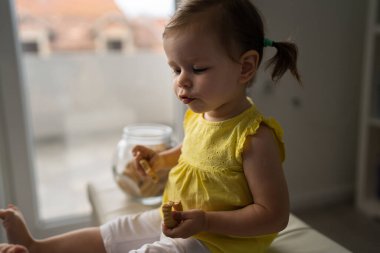 Bir küçük beyaz bebek evde oturup cam kavanozdan kurabiye yiyor ve çocukluk konseptini evde kopyalıyor.