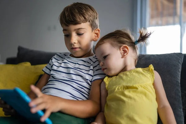 ある就学前の男の子座っています彼の妹とソファの上に自宅で見ますデジタルタブレットゲームをプレイしています — ストック写真
