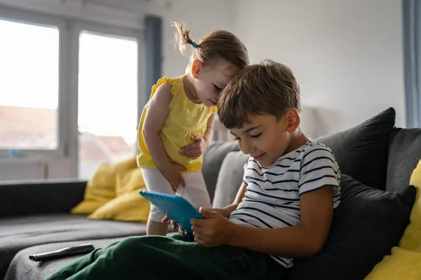 brother and sister small caucasian child siblings boy using digital tablet to play video games at home