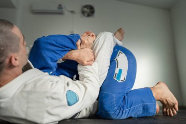 Brezilya jiu jitsu bjj eğitimi ya da iki sporcuyu serbest bırakmak spor salonunda tatami minderlerin üzerinde diyet dövüş sanatları tekniği kimono gi siyah kuşak eğitmeni olarak kimura sunumunu gösterin.