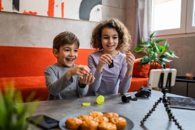 Erkek ve kız kardeş iki kardeş cep telefonuyla video blogu yapıyorlar evlerinden internet günlüğü için en sevdikleri oyuncak eleştirisi hakkında sosyal ağ kopyalama alanı için içerik oluştur ve paylaş