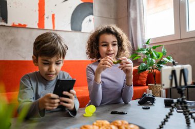 Erkek ve kız kardeş iki kardeş cep telefonuyla video blogu yapıyorlar evlerinden internet günlüğü için en sevdikleri oyuncak eleştirisi hakkında sosyal ağ kopyalama alanı için içerik oluştur ve paylaş