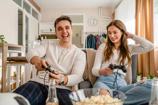 2人の白人の人々座っていますホームプレイビデオゲームコンソール楽しいカップル男と女のボーイフレンドとガールフレンドを持っています一緒に時間を過ごしますジョイスティックコントローラー笑顔フロントビュー — ストック写真