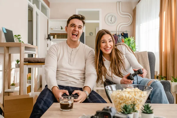 2人の白人の人々座っていますホームプレイビデオゲームコンソール楽しいカップル男と女のボーイフレンドとガールフレンドを持っています一緒に時間を過ごしますジョイスティックコントローラー笑顔フロントビュー — ストック写真